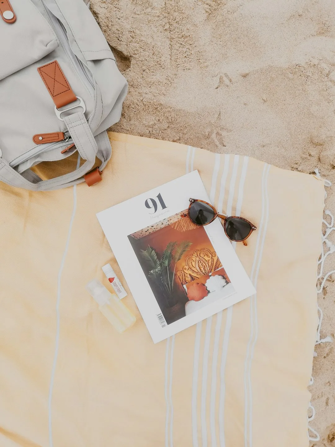 A woven beach bag resting on pale sand beside a folded quick-dry towel